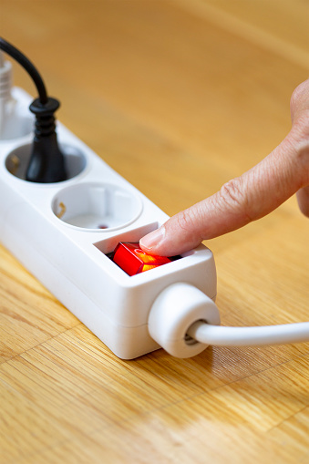 Pressing red button of a white power strip on wooden background - energy saving
