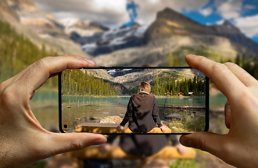 Tourist taking a picture with a mobile phone of a man resting on a bench at the Lake O'Hara, Yoho National Park.