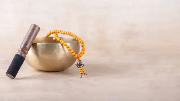 Photo of Tibetan singing bowl with stick, mala beads strands used during mantra meditations on beige stone background