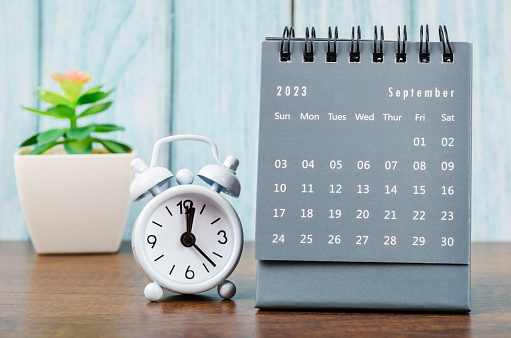 El calendario de escritorio mensual de septiembre de 2023 para el año 2023 con despertador sobre fondo de madera azul. photo