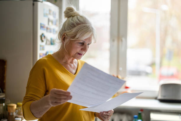 mujer mayor llenando estados financieros - senior mujer leyendo documentos fotografías e imágenes de stock