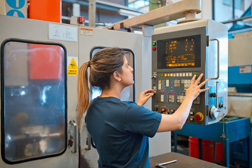 Side view of female technician wearing navy blue t-shirt using machinery in factory.