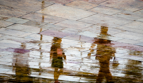 Abstract blurry silhouette reflections of unrecognizable people walking on wet city street pavement on a rainy day