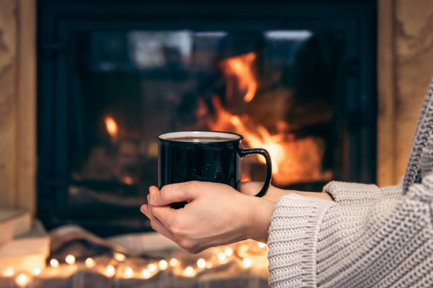 istock A cup with a hot drink in female hands on a blurred fireplace background. 1446919776