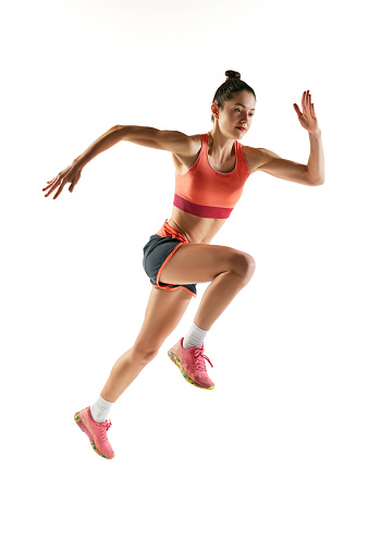 Big energy and speed. Athlete in motion. Young fitness sportive girl in sports uniform running, training isolated over white background. Dynamic movements, running technique.