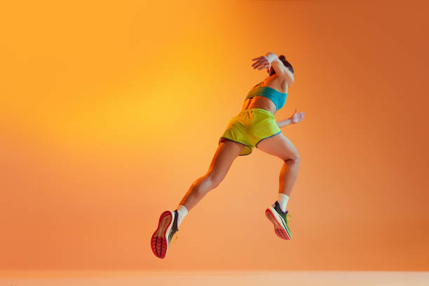 Back view. Sportive muscled woman, professional runner running away isolated on orange background in noen light. Sport, fitness, competition, speed and ad Back view. Sportive muscled woman, professional runner running away isolated on yellow background in neon light. Sport, fitness, competition, speed and active lifestyle. Copy space for ad. Sunset scoring run stock pictures, royalty-free photos & images