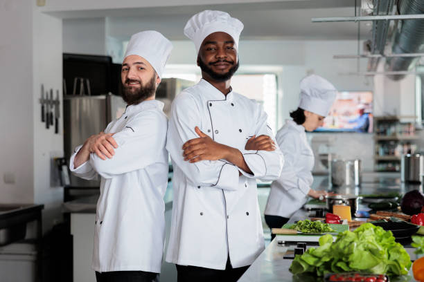 istock Food industry workers standing back to back while looking at camera in restaurant kitchen space. 1446920198