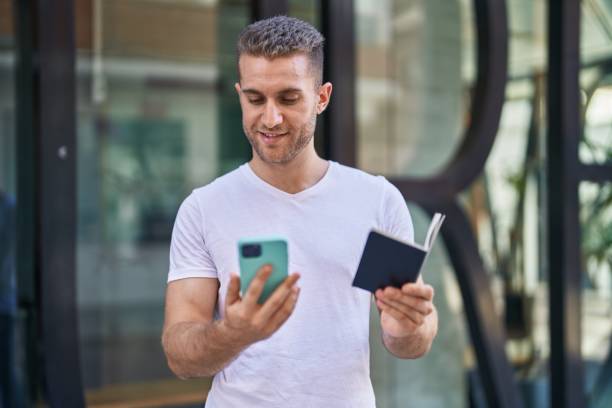 istock Young caucasian man using smartphone holding passport at street 1446920556