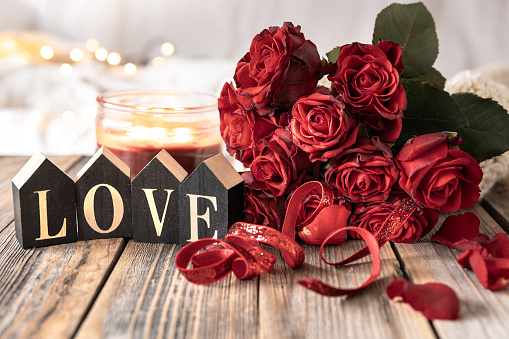 Festive background for Valentine's Day with a bouquet of red roses and decorative wooden word love.