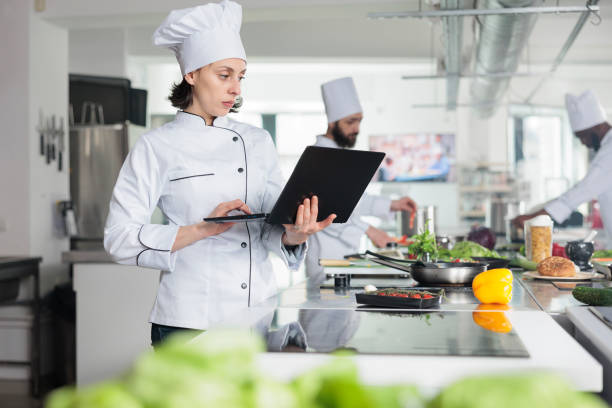 istock Sous chef with modern laptop looking for gourmet dish recipe while standing in restaurant professional kitchen. 1446921185