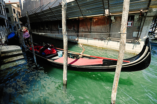 Venice, Italy - July 04, 2022: Gondolier dressed in traditional striped top and straw hat with red ribbon in his gondola on Grand Canal, Venice.