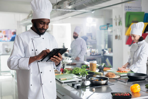 istock Head chef with modern touchscreen tablet device searching for gourmet cuisine dish recipe 1446921869