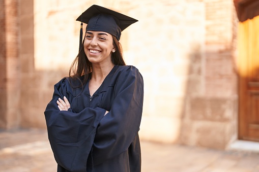 Young hispanic woman wearing graduated uniform standing with arms crossed gesture at university