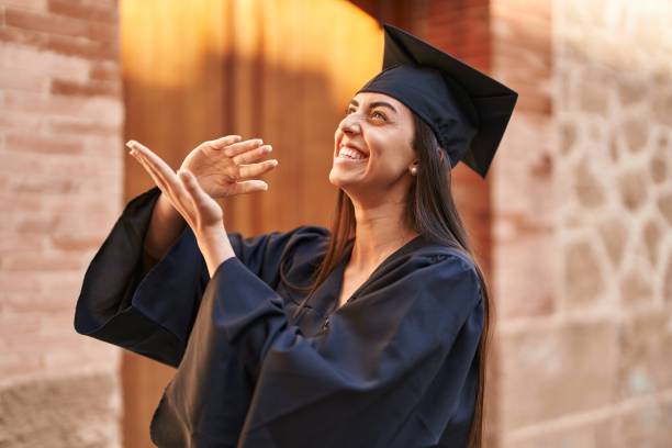 une jeune femme hispanique portant l’uniforme des diplômés fait un geste de dépenser de l’argent avec les mains à l’université - women business graduation casual photos et images de collection