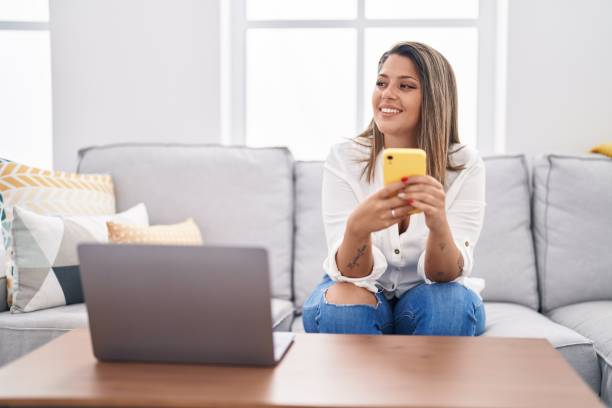 istock Young hispanic woman using smartphone sitting on sofa at home 1446922699