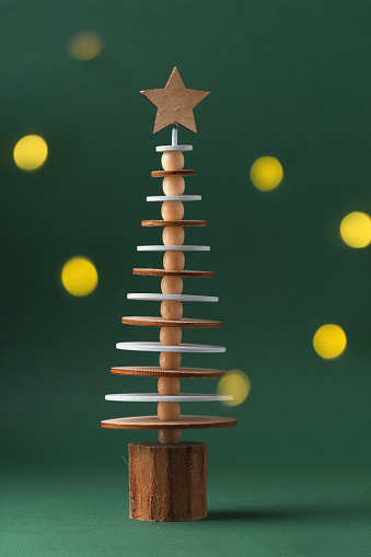 Wooden toy in the shape of Christmas tree with the star on top. Dark green festive background with warm bokeh blurred lights. Close-up