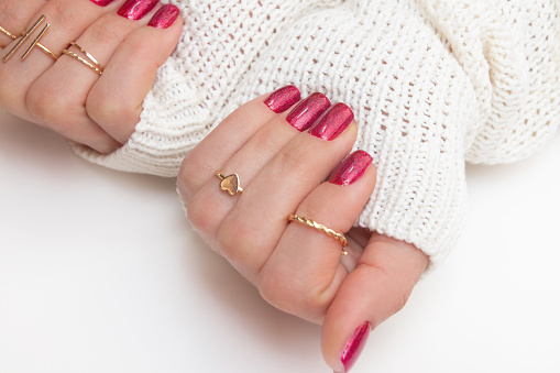 Manicure gel polish of viva magenta color with sparkles on female fingers with rings.