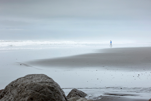 white man in blue winter coat walking on one of black sand beaches along Iceland's south coast