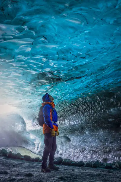 Photo of man standing in a beautiful blue ice cave of the Vatnajökull glacier in Iceland