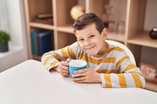 Blond child drinking milk sitting on table at home