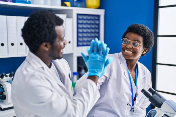 african american man and woman scientists high five with hands raised up at laboratory - smiling research science and technology clothing imagens e fotografias de stock