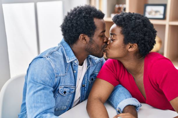 coppia di uomini e donne afroamericani che si siedono sul tavolo che si baciano a casa - couple black american culture kissing foto e immagini stock