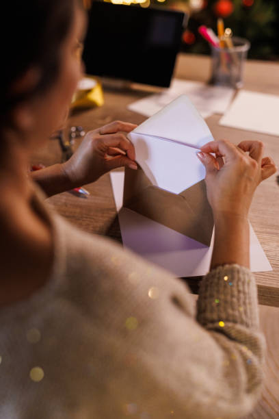 istock Woman putting a Christmas letter, that she wrote, in a gold colored envelope 1446926384