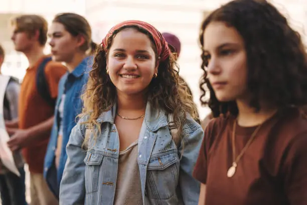 Happy teenage girl smiling at the camera while standing with a group of demonstrators in the city. Multicultural generation z activists marching for equality and social change.