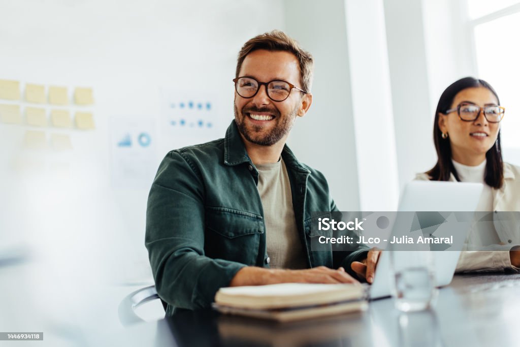 Happy business man listening to a discussion in an office Happy business man listening to a discussion in an office boardroom. Business professional sitting in a meeting with his colleagues. Office Stock Photo
