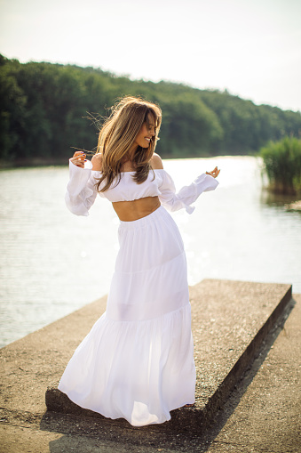 Beautiful mid adult woman is wearing a dress. She is attractive fashion model and she is enjoying in nature while dancing on summer day