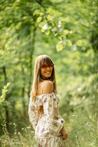 Beautiful mid adult woman is wearing a dress. She is attractive and happy fashion model and is enjoying in nature while posing on summer day