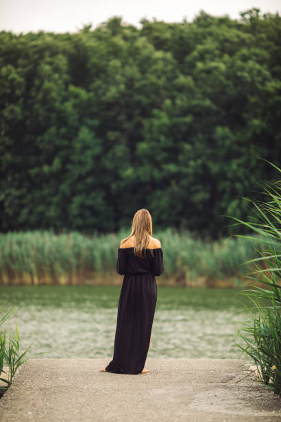 Beautiful mid adult woman is wearing a dress. She is attractive and she is enjoying in nature while looking away on summer day. Photo taken from her back