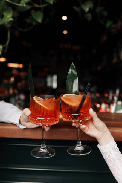 hands of woman and man are clinking, cheers with glasses of Spritz cocktail. Couple celebrating wedding, anniversary with Spritz cocktails, with orange and greens Refreshing alcoholic drink hands of woman and man are clinking, cheers with glasses of Spritz cocktail. Couple celebrating wedding, anniversary with Spritz cocktails, with orange and greens Refreshing alcoholic drink. crystal chalice stock pictures, royalty-free photos & images