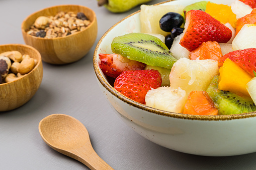 Fresh fruit salad in a bowl. Multicolored and tropical fruits. Pineapple, mango, grape, strawberry, papaya, melon, kiwi. Additional with chestnuts and granola. Selective focus.