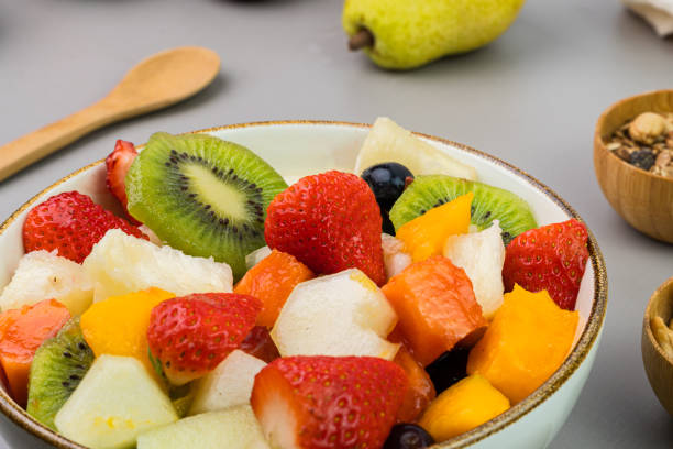 istock Fresh fruit salad in a bowl. Multicolored and tropical fruits. Pineapple, mango, grape, strawberry, papaya, melon, kiwi. Additional with chestnuts and granola. Selective focus 1446943301