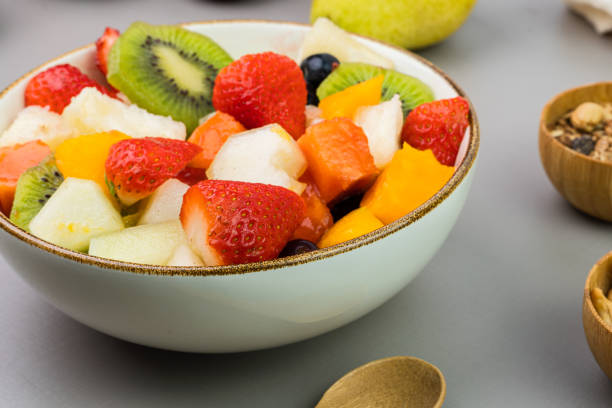 istock Fresh fruit salad in a bowl. Multicolored and tropical fruits. Pineapple, mango, grape, strawberry, papaya, melon, kiwi. Additional with chestnuts and granola. Selective focus 1446943318