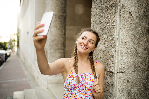 Portrait of a beautiful young woman enjoying in the city and taking a selfie