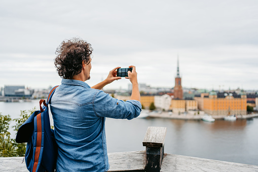 Handsome young man taking pictures of the old town Stockholm city at a high viewpoint.