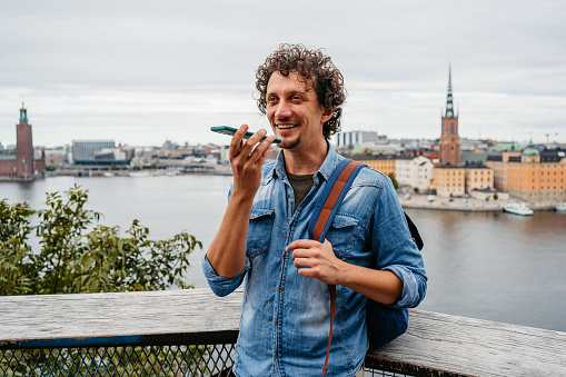 Handsome young man sending a voice message using phone in the city, at a high viewpoint in Stockholm, Sweden.