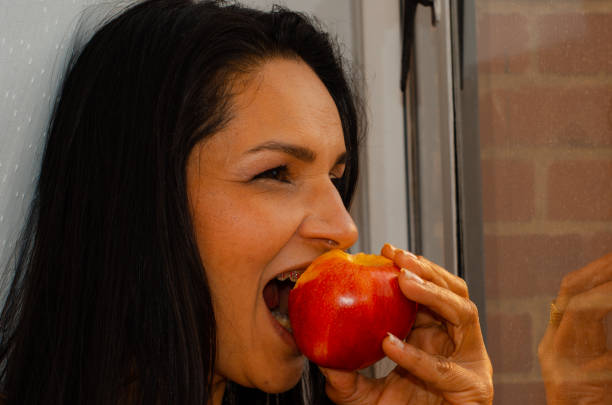 Woman biting a red apple next to a window