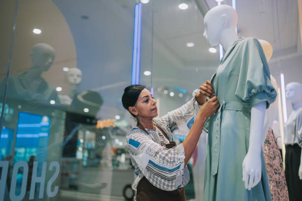 des femmes indiennes asiatiques exposent un artiste habillant un mannequin dans la vitrine d’un magasin de vêtements pour femmes - department store clothing showroom people photos et images de collection