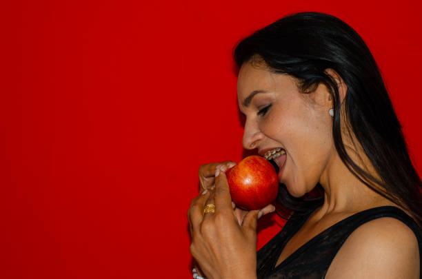 Woman biting a red apple with copy space and colored background