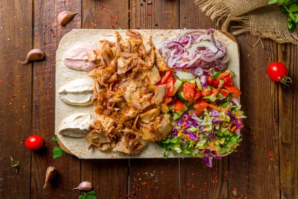 Shawarma with chicken and fresh vegetables on a board on wooden table top view