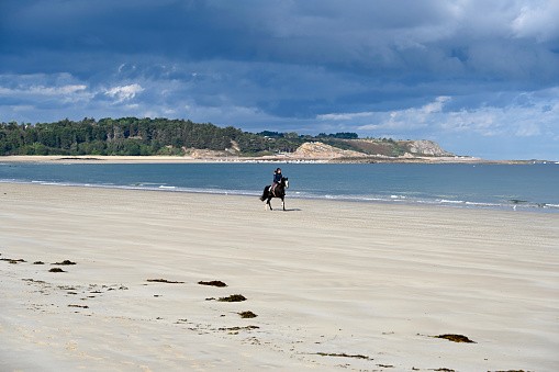 Erquy, France, September 19, 2022 - Young man enjoys horse riding on empty beach in Fréhel, Brittany.