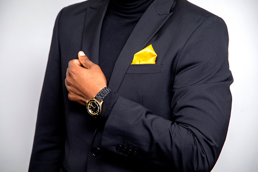 Close up of an African American wearing a black suit wearing a yellow handkerchief and a watch
