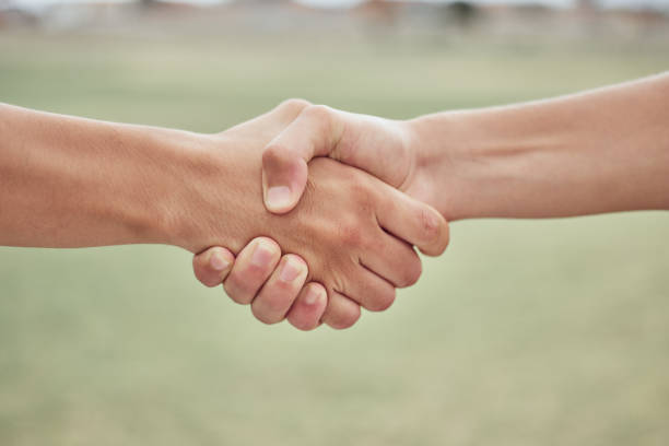 istock Closeup of two unknown baseball players shaking hands while standing on a grass field. Two sportsmen greeting or congratulating on a good game 1446950283