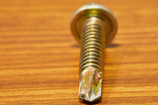 one bronze-colored self-tapping screw close-up, photographed standing on a wooden table