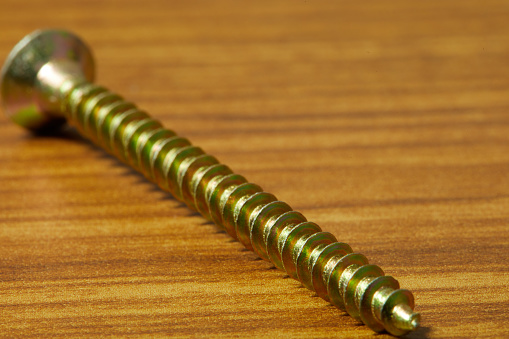 one bronze-colored screw close-up, photographed on a wooden table