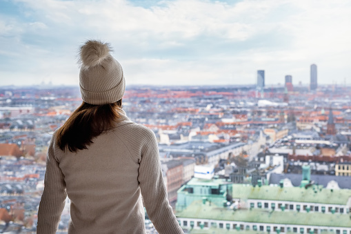 A tourist woman in winter clothing enjoys the elevated, panoramic view over the skyline of Copenhagen, Denmark, during a cold day