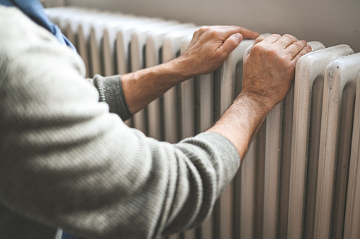 mature adult man warms himself by the radiator in the room